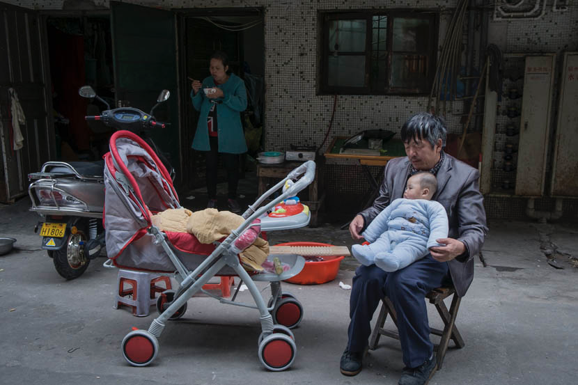 2015年3月，江西省凰岗镇，阿白的丈夫邹大哥在房门前和孩子玩耍，而阿白在吃午饭。图/丛妍