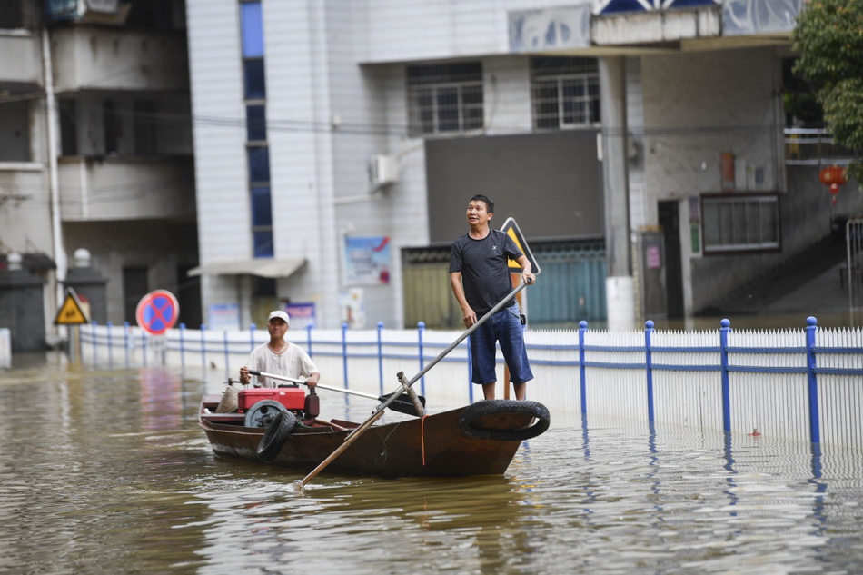 7月14日，在湖南永州冷水滩区杨家桥街道伍家院社区，志愿者唐新林（右）和唐满园（左）在被洪水淹没的道路上巡逻，查看是否有需要帮助的群众。