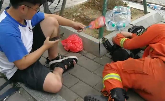 消防员中暑躺路边，市民坐地上为其扇风