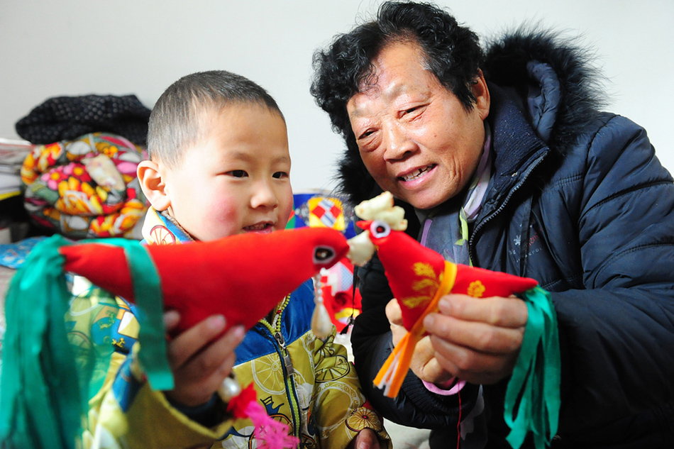 11.2017年2月3日，安徽省阜阳市的民间艺人张新荣（右）手拿缝制的民间传统手工艺“春鸡”给小朋友讲解“立春”节气的由来。