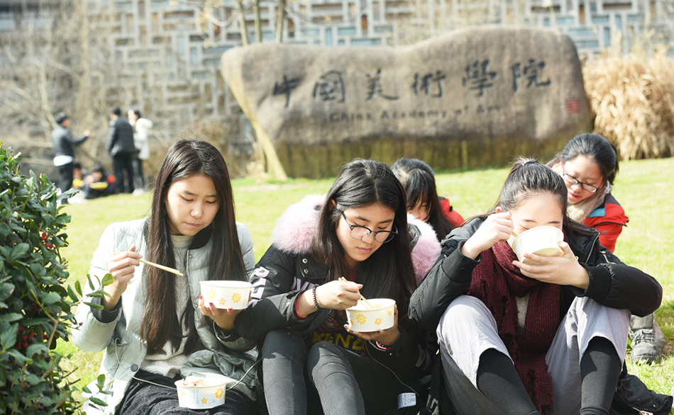 14.2017年2月7日，浙江省杭州市，参加中国美院艺考的考生在校门口吃着盒饭等待下午的考试。